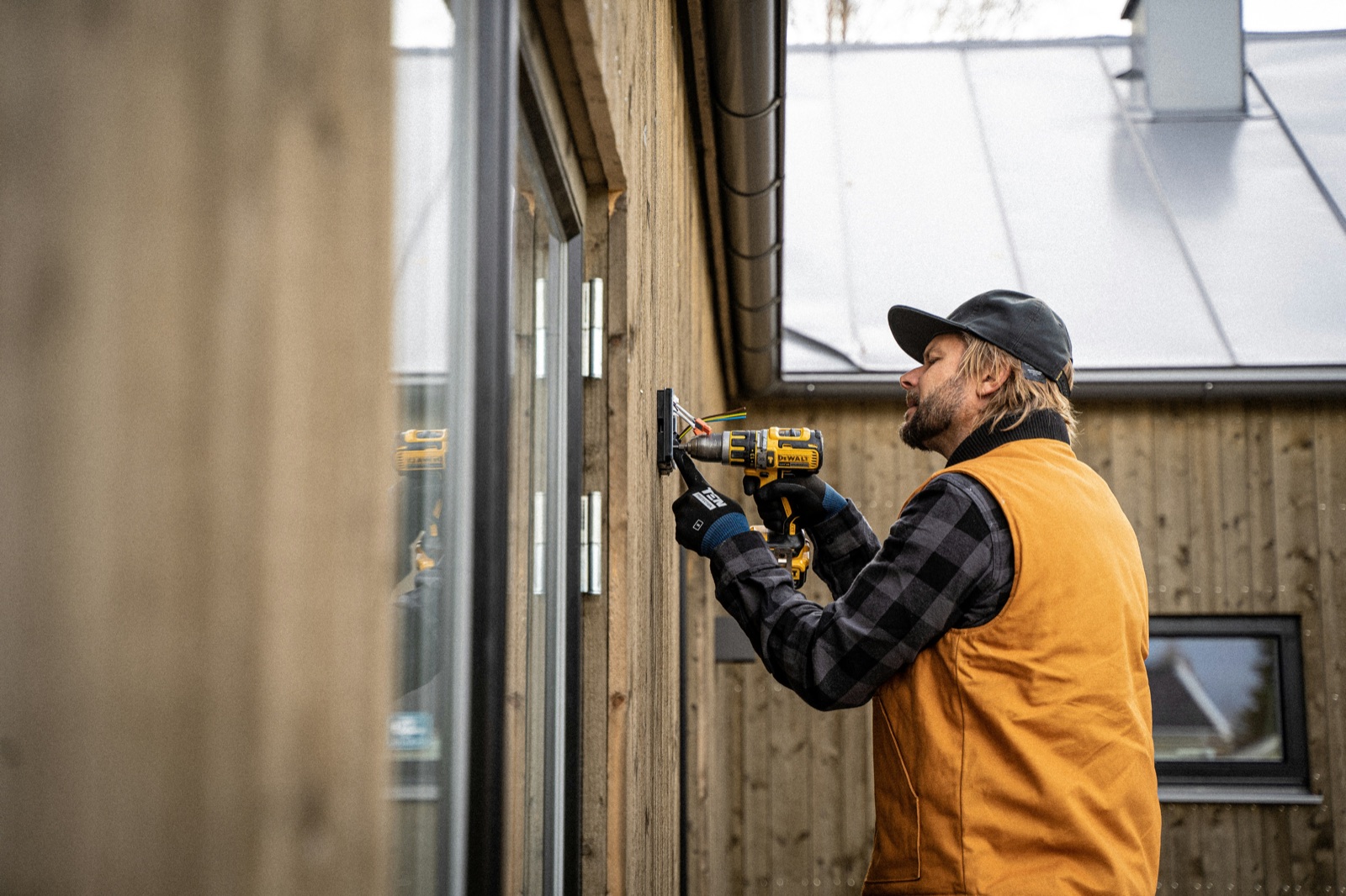 Elektriker monterar en eldosa på en träfasad.